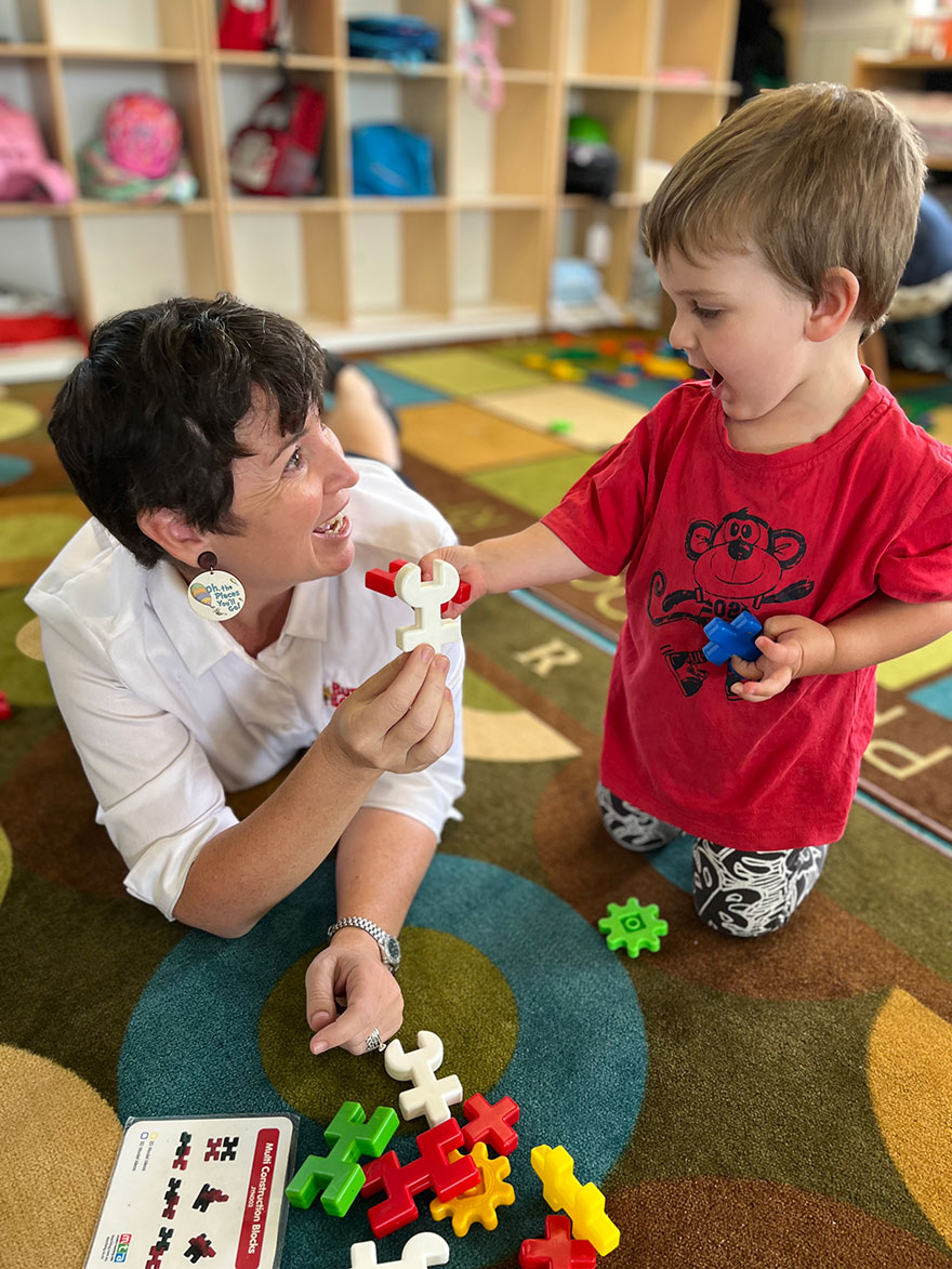 Child care worker playing with a toddler on the floor at a child care centre.