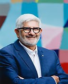 Head shot of Bill Louden - Smiling man with short grey hair and beard, wearing black framed glasses, a royal blue business jacket with white collared business shirt with his arms crossed.