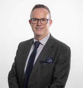 Mr Douglas Melrose-Rae headshot - smiling man with short brown hair, wearing black framed glasses, a dark grey business jacket, light collared business shirt and dark blue tie. 