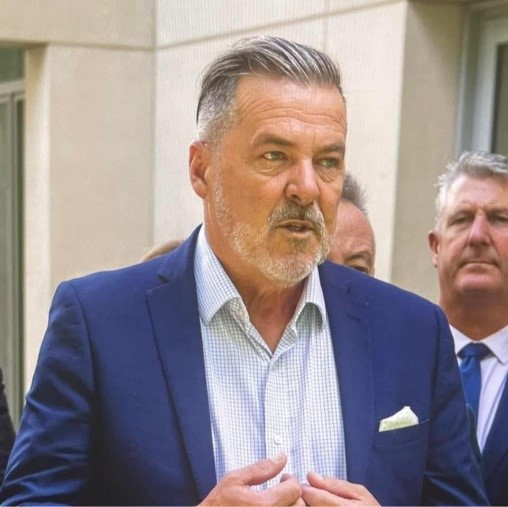 Headshot of Matthew Johnson - man with short grey hair and a goatee, wearing a royal blue business jacket, light, open necked business shirt and white pocket square.