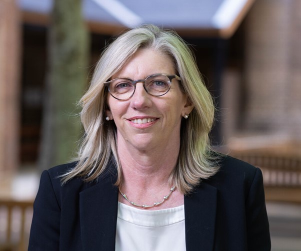 Head shot of Elizabeth Labone - smiling woman with shoulder length blonde hair, wearing glasses, a white round necked shirt and a black business jacket.