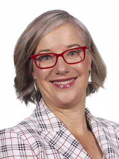 Alison Dell - headshot of a woman with light, straight shoulder length hair wearing red spectacles and a white, black and red jacket smiling.