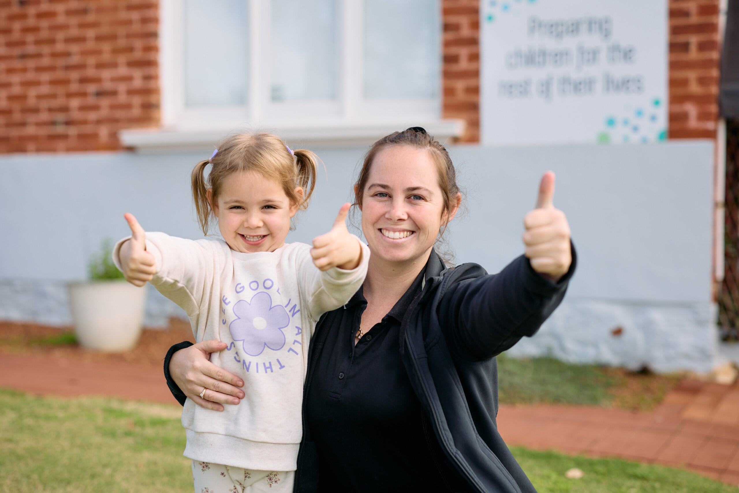 Young girl and woman sticking their thumbs up in an embrace