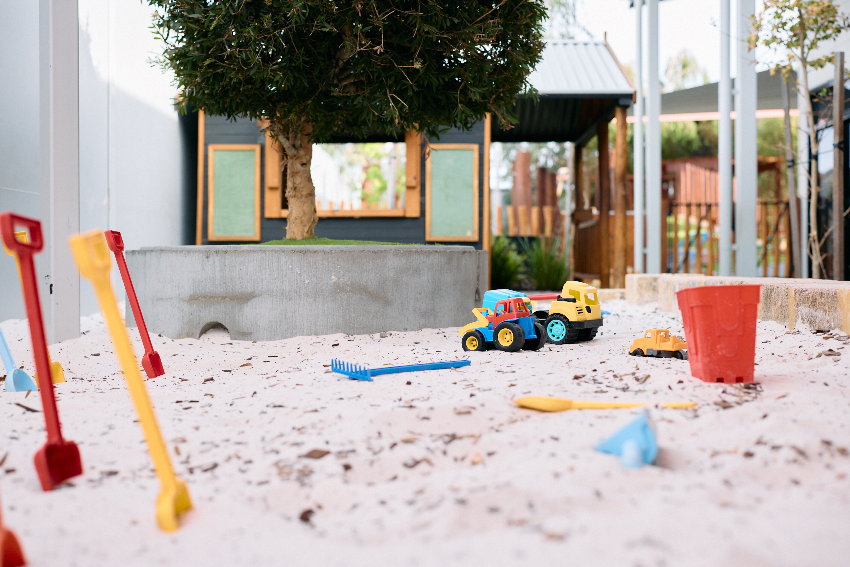 Image of a sand pit at a childcare facility with plastic spades, trucks and buckets.