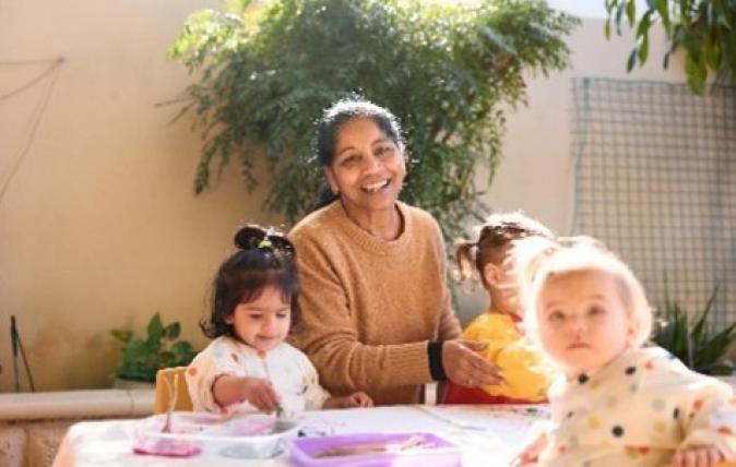 Child care worker sitting at a table with three children at a child care centre doing craft